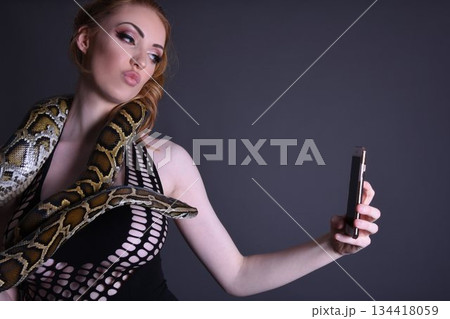 Beautiful redhead girl posing with her pet snake in the studio Beautiful redhead girl posing with her pet snake in the studio 134418059