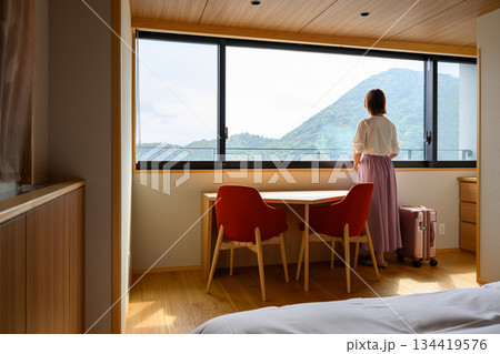 窓辺で山を望む女性とスーツケース 134419576