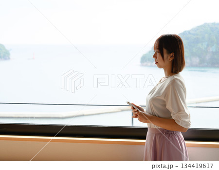窓辺で海を眺める女性とスマホ 134419617
