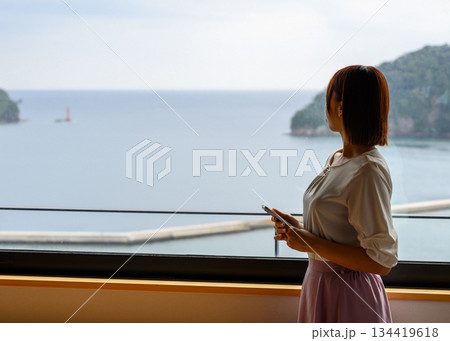 窓から海を眺める女性とスマホ 134419618