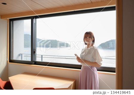 窓辺でスマホを持つ20代女性 134419645