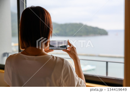 窓辺で景色をスマホ撮影する女性の後ろ姿 134419649