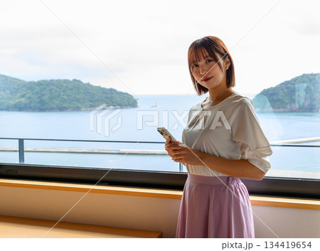 窓辺でスマホを持つ女性と海 134419654