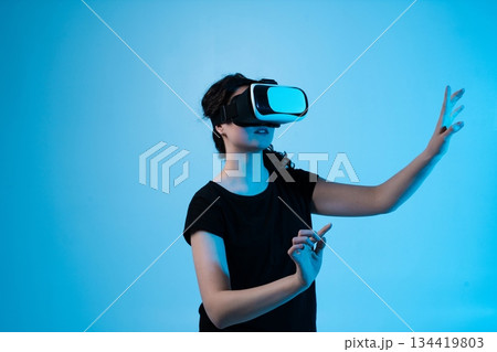 Woman interacting with virtual reality headset, exploring immersive digital interface Woman interacting with virtual reality headset, exploring immersive digital interface 134419803