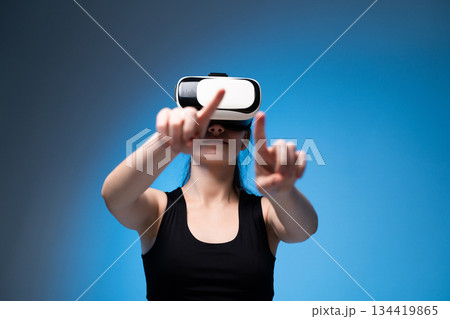 Young woman using VR headset with extended hands interacting with virtual controls in bright blue environment Young woman using VR headset with extended hands interacting with virtual controls in bright blue environment 134419865