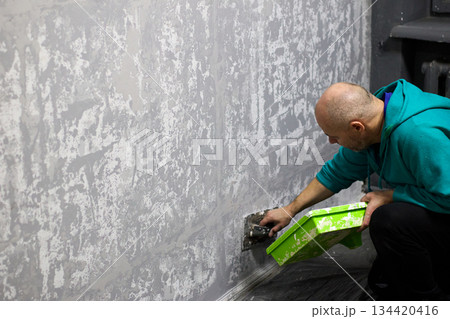 Man skillfully applies decorative plaster to a wall, enhancing the interior of an apartment 134420416