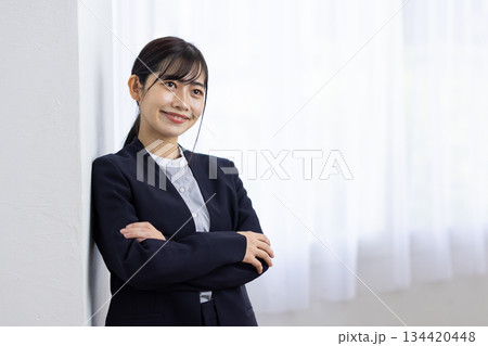 窓際で腕を組んで微笑むスーツ姿の若い女性 窓際で腕を組んで微笑むスーツ姿の若い女性 134420448