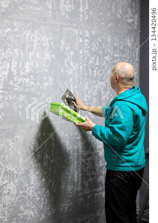 Professional plasterer expertly applies decorative plaster to a wall with a trowel 134420496