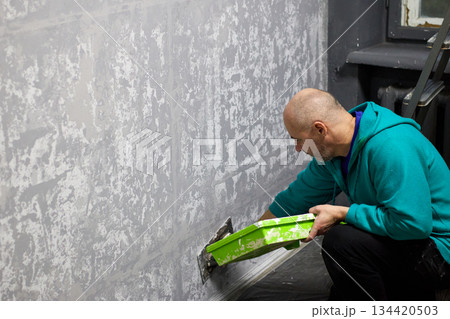 A skilled plasterer masterfully applies decorative plaster to a wall with a trowel A skilled plasterer masterfully applies decorative plaster to a wall with a trowel 134420503