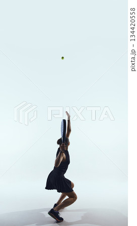 Padel player jumps upward hitting ball at peak height 134420558