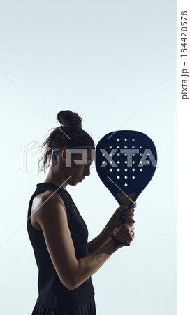 Focused female padel athlete holding racket before serve on white background. Focused female padel athlete holding racket before serve on white background. 134420578