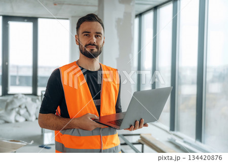 Silver colored laptop in hands. A man is renovating an unfinished room Silver colored laptop in hands. A man is renovating an unfinished room 134420876
