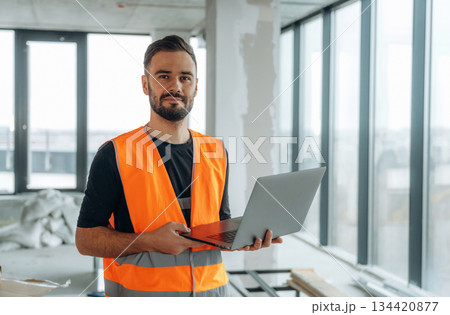 Silver colored laptop in hands. A man is renovating an unfinished room Silver colored laptop in hands. A man is renovating an unfinished room 134420877