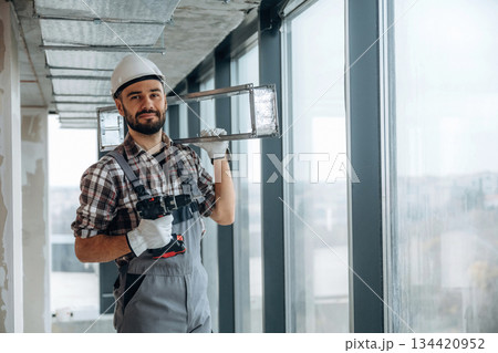 Handyman is with drill and metal piece for ceiling. A man is renovating an unfinished room 134420952
