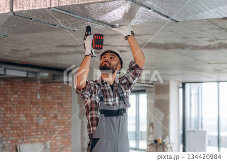 Hands are up, ceiling work. A man is renovating an unfinished room Hands are up, ceiling work. A man is renovating an unfinished room 134420984
