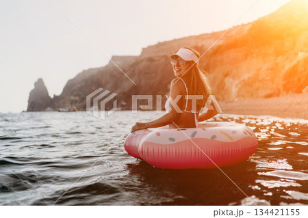 Woman, ocean, donut float, happy woman enjoying summer vacation in clear sea near cliffs with copy space. 134421155