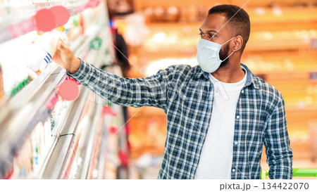 Grocery Shopping. African American Guy Wearing Face Mask Buying Food In Local Supermarket Standing With Shopping Cart Indoor. Male Consumer Choosing Groceries In Store During Quarantine Grocery Shopping. African American Guy Wearing Face Mask Buying Food In Local Supermarket Standing With Shopping Cart Indoor. Male Consumer Choosing Groceries In Store During Quarantine 134422070