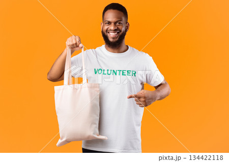 No Plastic. African Male Volunteer Pointing At White Eco Bag Standing On Yellow Studio Background. Ecology And Plastic-Free Consumerism, Eco-Friendly Lifestyle Concept No Plastic. African Male Volunteer Pointing At White Eco Bag Standing On Yellow Studio Background. Ecology And Plastic-Free Consumerism, Eco-Friendly Lifestyle Concept 134422118