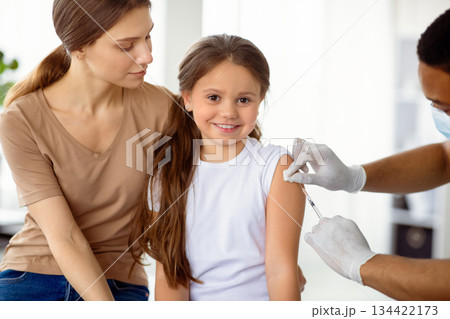 Cute happy girl visiting doctor with her mom, getting injection of covid-19 vaccine at hospital. Parent and child receiving immunization against coronavirus at clinic. Protection against viral disease Cute happy girl visiting doctor with her mom, getting injection of covid-19 vaccine at hospital. Parent and child receiving immunization against coronavirus at clinic. Protection against viral disease 134422173