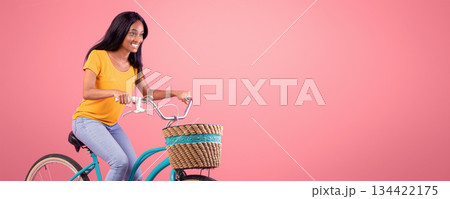 Portrait of pretty African American lady riding vintage bike over pink studio background. Happy black woman on bicycle going for ride. Active lifestyle, tourism and sports concept Portrait of pretty African American lady riding vintage bike over pink studio background. Happy black woman on bicycle going for ride. Active lifestyle, tourism and sports concept 134422175