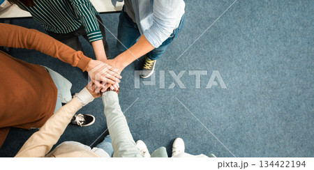 Teamwork And Unity Concept. Above top high angle view of young diverse group of people putting hands together standing in circle, celebrating collaboration and alliance. Panorama, banner, free space Teamwork And Unity Concept. Above top high angle view of young diverse group of people putting hands together standing in circle, celebrating collaboration and alliance. Panorama, banner, free space 134422194