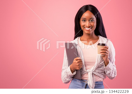 Attractive black lady with laptop computer and takeaway coffee looking at camera on pink studio background. Portrait of African American woman with modern gadget and hot drink posing and smiling Attractive black lady with laptop computer and takeaway coffee looking at camera on pink studio background. Portrait of African American woman with modern gadget and hot drink posing and smiling 134422229