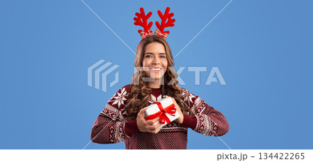 Winter holiday shopping. Pretty millennial girl in Christmas clothes holding gift box on blue background Winter holiday shopping. Pretty millennial girl in Christmas clothes holding gift box on blue background 134422265