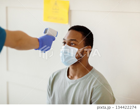 Young black man having his temperature measured by infrared thermometer at clinic before getting covid-19 vaccine injection. Population immunization and health service concept Young black man having his temperature measured by infrared thermometer at clinic before getting covid-19 vaccine injection. Population immunization and health service concept 134422274