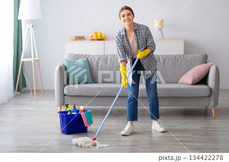 Pretty young lady wiping floor with mop, doing house cleanup, free space. Positive housewife tidying her apartment, doing household chores. Professional sanitary service concept Pretty young lady wiping floor with mop, doing house cleanup, free space. Positive housewife tidying her apartment, doing household chores. Professional sanitary service concept 134422278