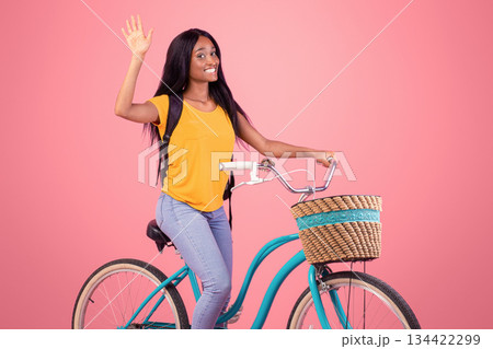 Active hobbies concept. Beautiful African American woman with bicycle smiling, looking at camera and waving on pink studio background. Happy black lady going for bike ride, enjoying sports Active hobbies concept. Beautiful African American woman with bicycle smiling, looking at camera and waving on pink studio background. Happy black lady going for bike ride, enjoying sports 134422299