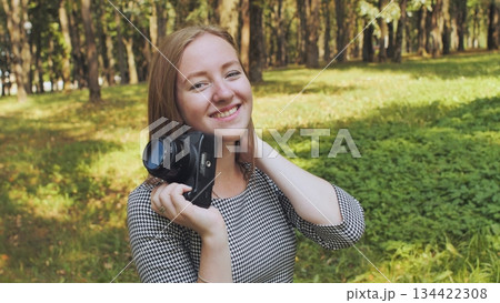 Female photographer smiling, holding camera during sunny park day, surrounded by verdant landscape and trees Female photographer smiling, holding camera during sunny park day, surrounded by verdant landscape and trees 134422308