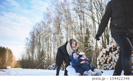 Smiling family sledding down snow covered hill, sharing laughter and winter excitement during outdoor recreational moment Smiling family sledding down snow covered hill, sharing laughter and winter excitement during outdoor recreational moment 134422346