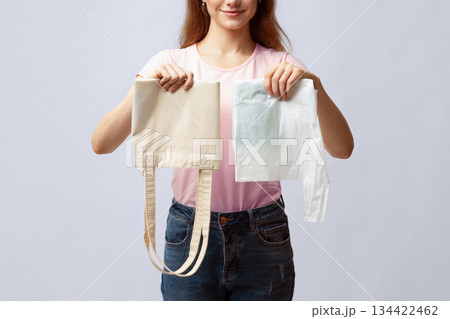 Zero Waste Shopping Concept. Unrecognizable Woman Holding Reusable Eco Bag In One Hand And Plastic Polyethylene Bag In Another While Standing Over Gray Studio Background, Cropped Image, Closeup Zero Waste Shopping Concept. Unrecognizable Woman Holding Reusable Eco Bag In One Hand And Plastic Polyethylene Bag In Another While Standing Over Gray Studio Background, Cropped Image, Closeup 134422462