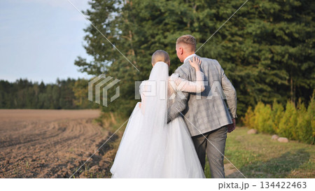 Newlyweds holding hands, walking through lush green landscape, sharing intimate moment after wedding ceremony 134422463