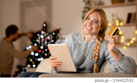 Cheerful wife buying Christmas gift for her husband online, using digital tablet and credit card, copy space. Happy woman purchasing online, holding pad and card for payments, buying presents Cheerful wife buying Christmas gift for her husband online, using digital tablet and credit card, copy space. Happy woman purchasing online, holding pad and card for payments, buying presents 134422532