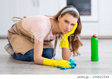 Upset young lady in rubber gloves and apron washing floor at kitchen, disliking house chores, feeling tired and unhappy, copy space. Millennial lady cleaning her house, suffering from ocd disorder 134422544