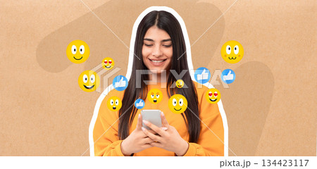 A young woman smiles while texting on her smartphone in a casual setting. Colorful emojis surround her, reflecting a joyful interaction on social media. A young woman smiles while texting on her smartphone in a casual setting. Colorful emojis surround her, reflecting a joyful interaction on social media. 134423117