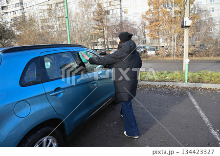 Person cleaning car windows in a parking lot during winter morning Person cleaning car windows in a parking lot during winter morning 134423327