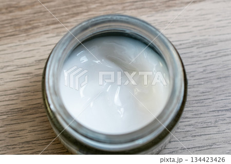 Open Jar of White Skincare Cream on a Wooden Surface 134423426