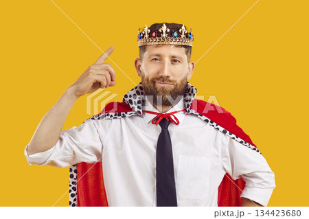 Cocky businessman shows his power by pointing his finger at crown on his head. Cocky businessman shows his power by pointing his finger at crown on his head. 134423680