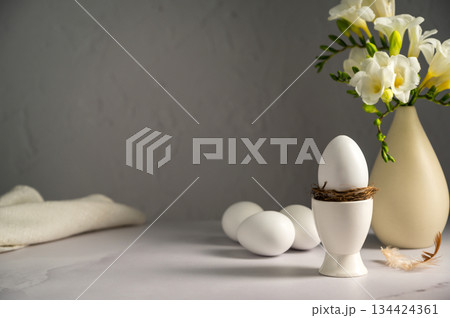 Spring, Easter background. White freesias flowers in a vase with white eggs. Copy space Spring, Easter background. White freesias flowers in a vase with white eggs. Copy space 134424361