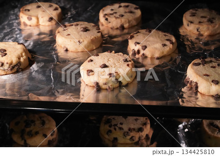 Chocolate chip cookies are laid out on a foil-lined baking sheet and baked in the oven in a checkerboard pattern. The process of baking homemade cookies. Close up. Horizontal, contrast photo. Chocolate chip cookies are laid out on a foil-lined baking sheet and baked in the oven in a checkerboard pattern. The process of baking homemade cookies. Close up. Horizontal, contrast photo. 134425810