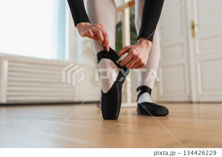 Ballerina puts on pointe shoes on leg in dance class. Classical ballet dancer woman in dance studio. Ballerina putting on tying classical pointe shoes for dance training. Ballet school concept Ballerina puts on pointe shoes on leg in dance class. Classical ballet dancer woman in dance studio. Ballerina putting on tying classical pointe shoes for dance training. Ballet school concept 134426229