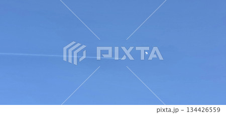 Airplane contrail in clear blue sky with moon visible in distance Airplane contrail in clear blue sky with moon visible in distance 134426559