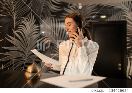 Receptionist talking on the phone while arranging accommodation for the customer Receptionist talking on the phone while arranging accommodation for the customer 134426624