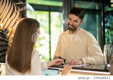 Receptionist talking to a male customer and arranging accommodation for him 134426631