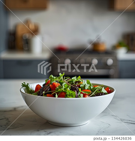 A close-up of a bowl of fresh green salad on a wooden table in a modern kitchen interior. Concepts of healthy eating, healthy lifestyle, home cooking and well-being, and post-holiday diet. 134426836