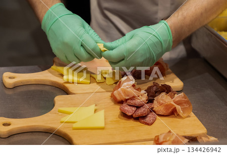 Culinary expert preparing assorted meats and cheeses on wooden cutting boards Culinary expert preparing assorted meats and cheeses on wooden cutting boards 134426942