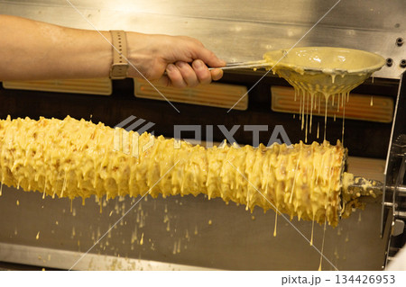 Hand holding spoon pouring golden syrup over spinning pastry cone 134426953