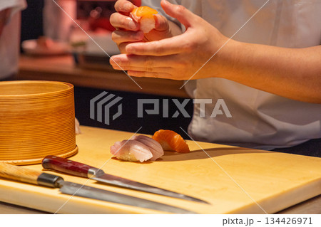 Sushi chef preparing fresh sushi rolls with precision and skillful hands 134426971